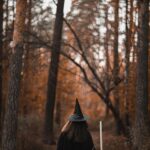 Woman in witch costume walking through an autumn forest with vibrant leaves.