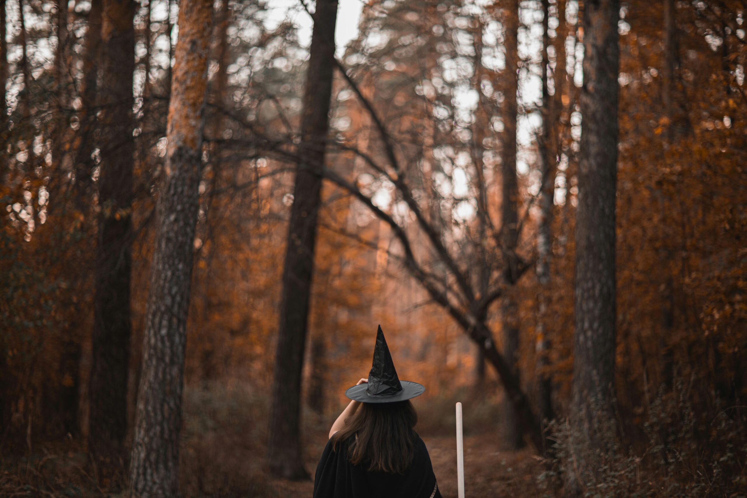 Woman in witch costume walking through an autumn forest with vibrant leaves.