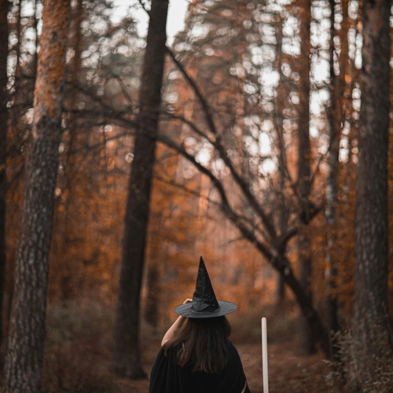Woman in witch costume walking through an autumn forest with vibrant leaves.